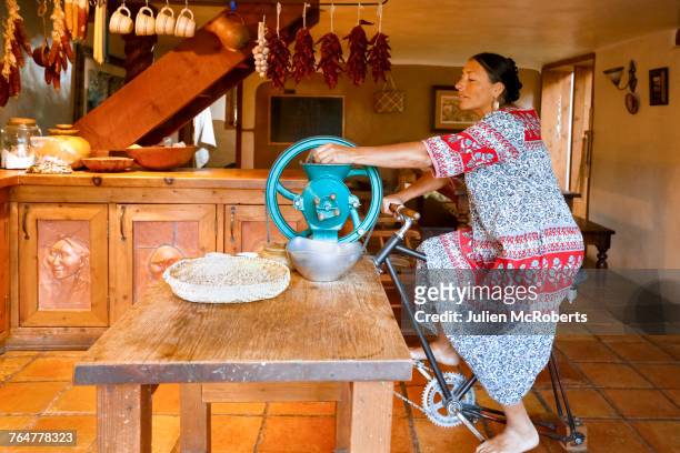 woman pedaling to power grinder in kitchen - pueblo stock-fotos und bilder