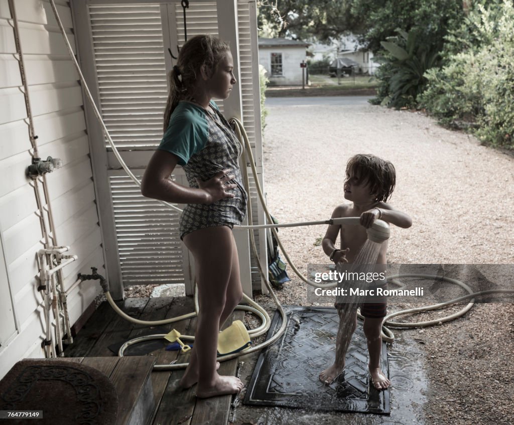 Frustrated Caucasian girl watching brother using shower outdoors