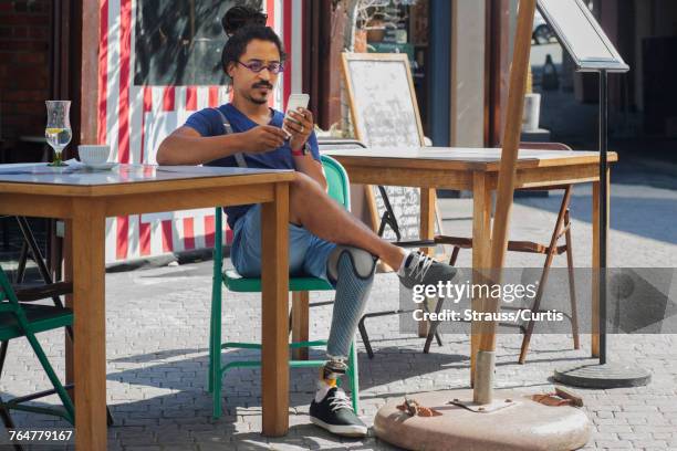 Mixed race man with prosthetic leg texting on cell phone at sidewalk cafe