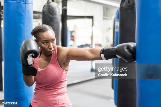 black woman wearing boxing gloves hitting punching bag - boxing bag stock pictures, royalty-free photos & images