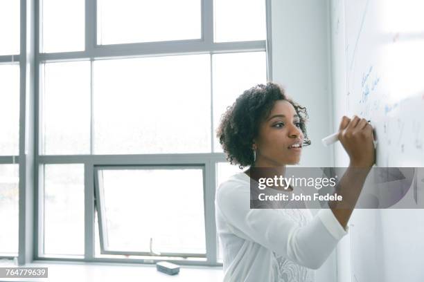 african american businesswoman writing on whiteboard in meeting - one young woman only photos et images de collection