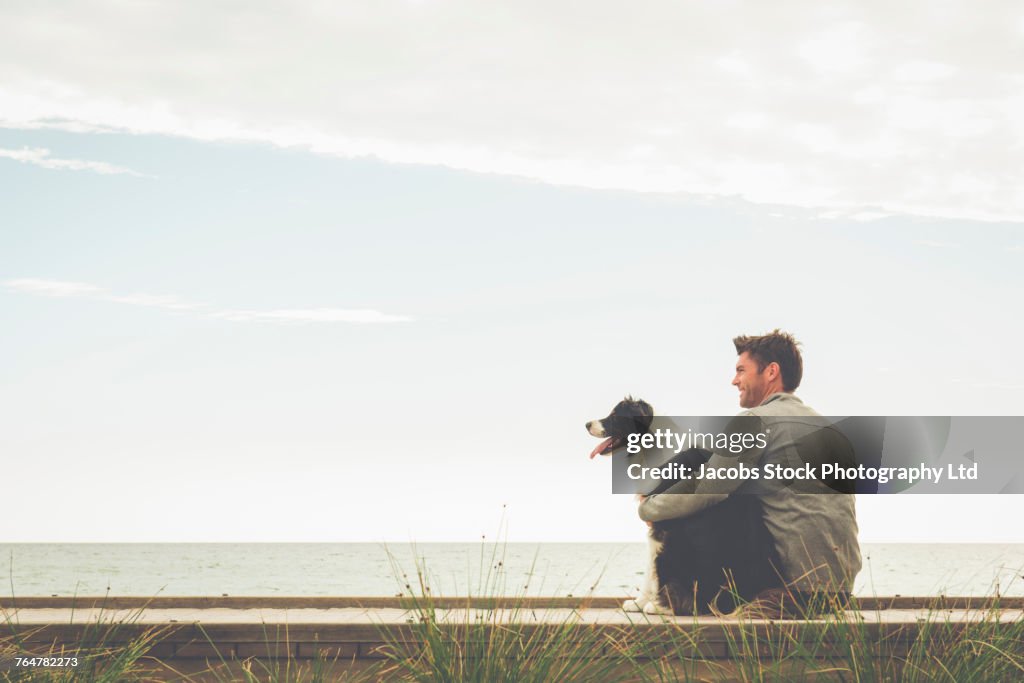 Caucasian man and dog sitting on boardwalk