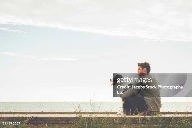 caucasian man and dog sitting on boardwalk - man and dog stock pictures, royalty-free photos & images