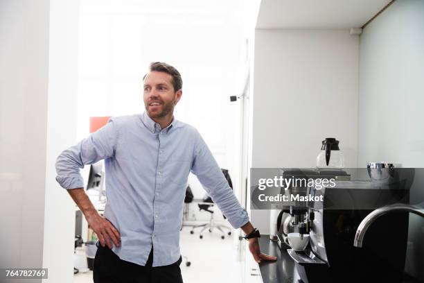 businessman standing by coffee maker at counter in creative office - man and machine fotografías e imágenes de stock