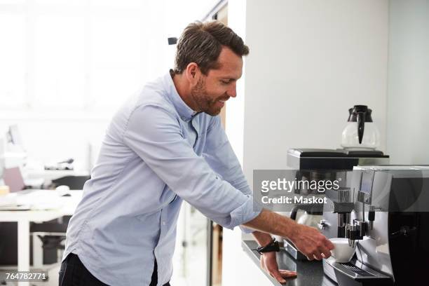 businessman using coffee maker at kitchen counter in creative office - kaffeemaschine stock-fotos und bilder