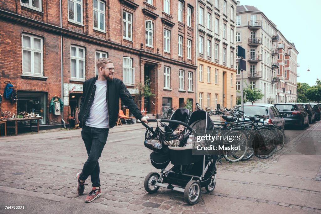 Full length of father standing by baby carriage on street in city