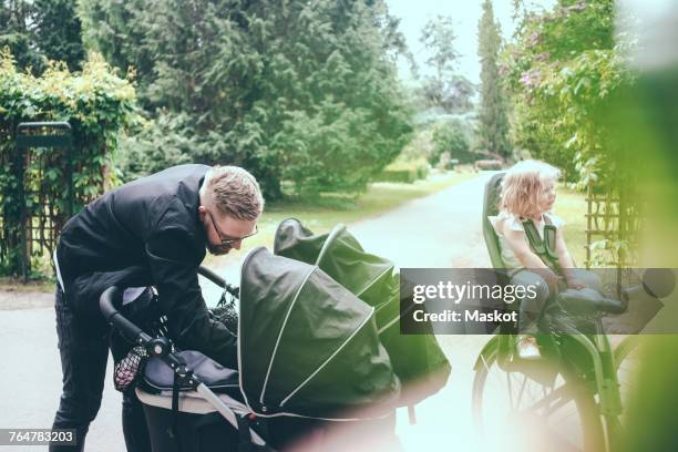 father peeking in baby carriage on footpath during sunny day - fokus-auf-den-hintergrund stock-fotos und bilder