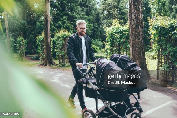 full length of man pushing baby carriage on footpath - carriage stock pictures, royalty-free photos & images