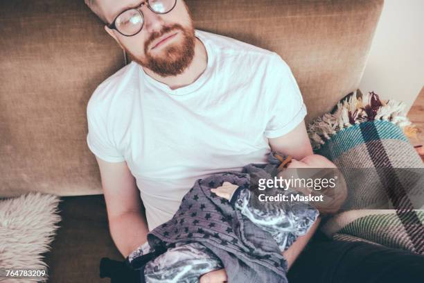 high angle view of man sleeping while holding baby boy on sofa - baby accessories the dummy stock pictures, royalty-free photos & images