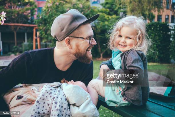 happy father looking at daughter while holding son in park - babyhood photos et images de collection