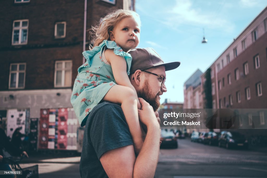Side view of father carrying daughter on shoulders at city street