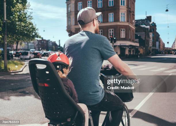 rear view of father cycling while daughter sitting on back seat at city street - bicycle daughter stock-fotos und bilder