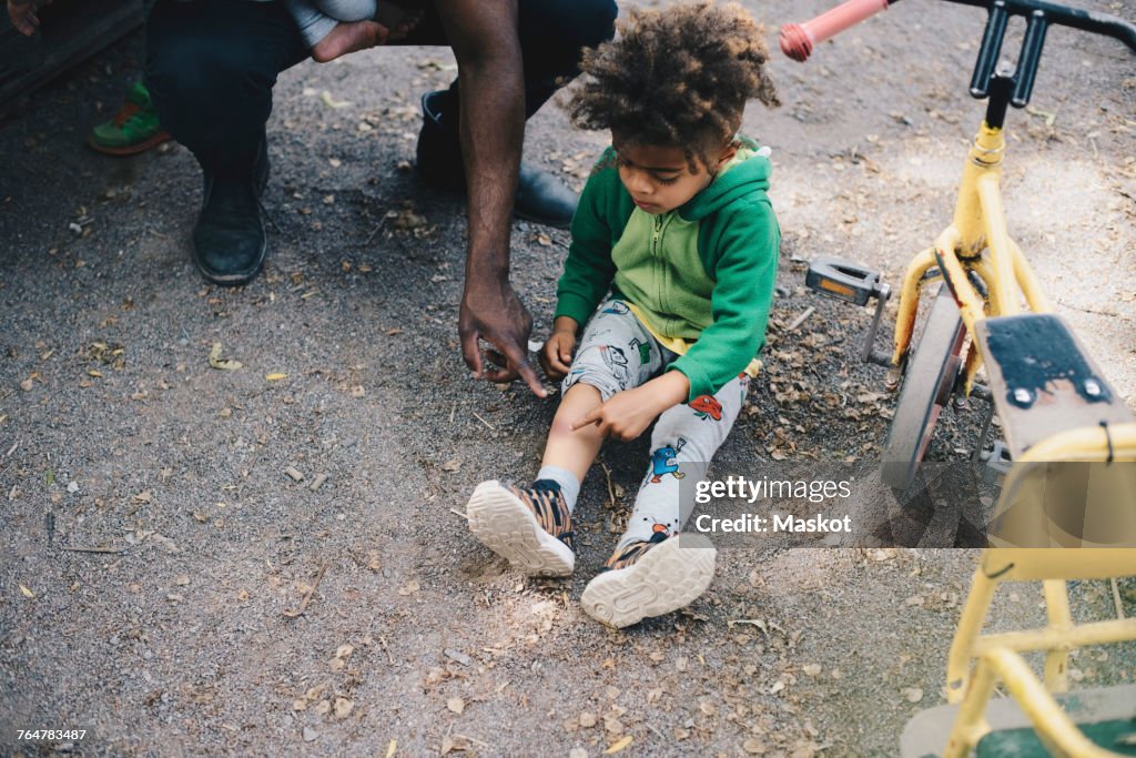 High angle view of son showing bruise to father while sitting by tricycle at park