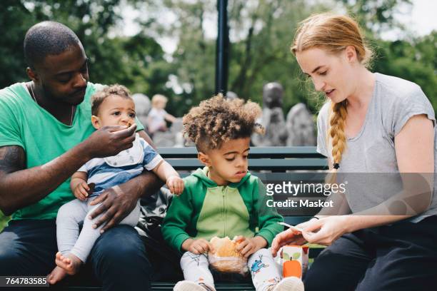 Parents having food with children while sitting on bench at park