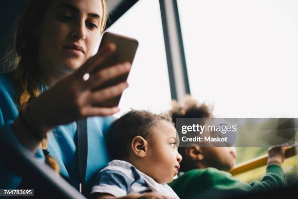 mother using mobile phone while sitting with son in bus - city bus stock pictures, royalty-free photos & images