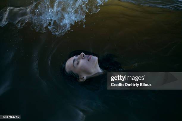 caucasian woman floating in ocean with eyes closed - ahogarse fotografías e imágenes de stock