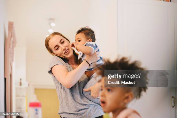 mother carrying son while talking on phone with boy sitting in foreground - multitasking mom stock pictures, royalty-free photos & images
