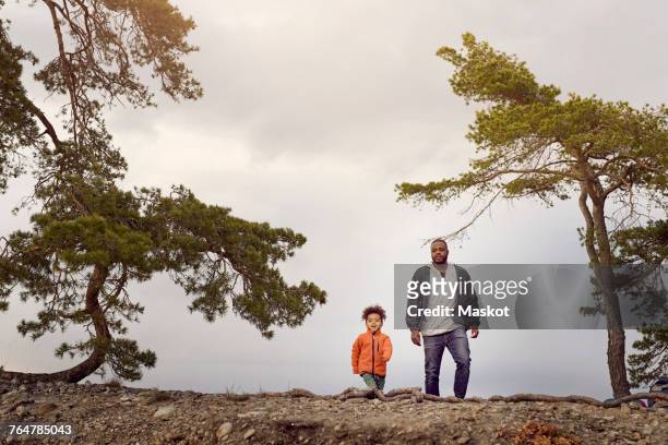 Father and son walking amidst trees against sky