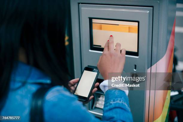 rear view of teenage girl touching atm screen while holding smart phone - atm screen stock-fotos und bilder