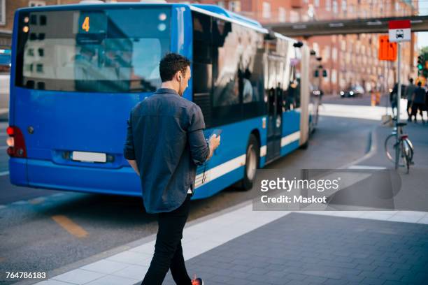 rear view of mid adult man walking on sidewalk while using mobile phone in city - bus lane stockfoto's en -beelden