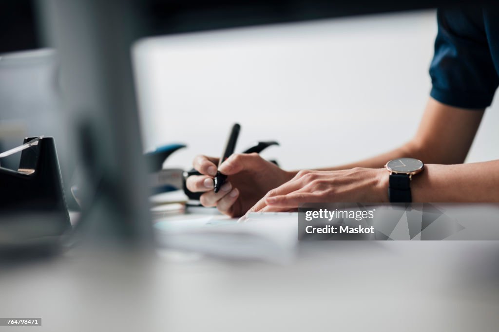 Cropped image of businesswoman writing at desk in office