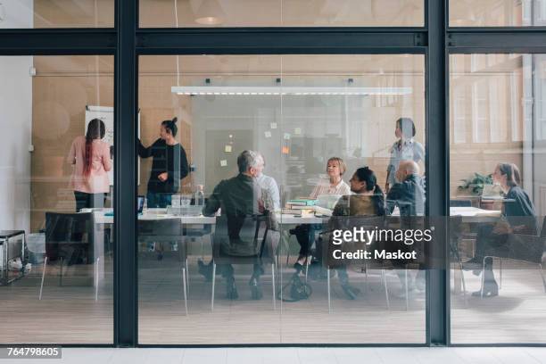 multi-ethnic business team sitting in board room at office seen from glass - office glas stock-fotos und bilder