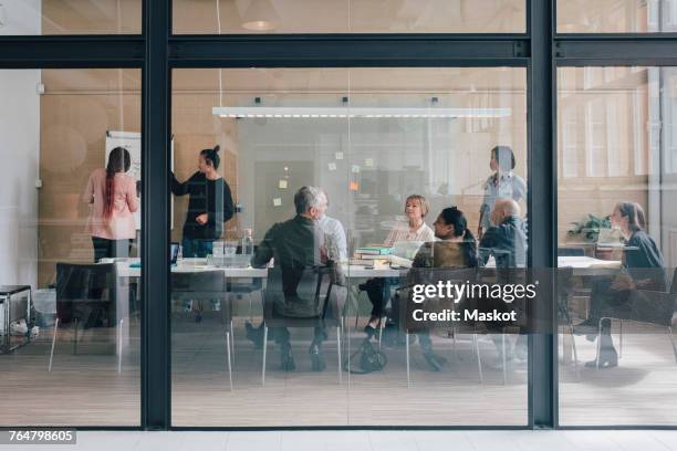 multi-ethnic business team sitting in board room at office seen from glass - glass meeting room stock pictures, royalty-free photos & images