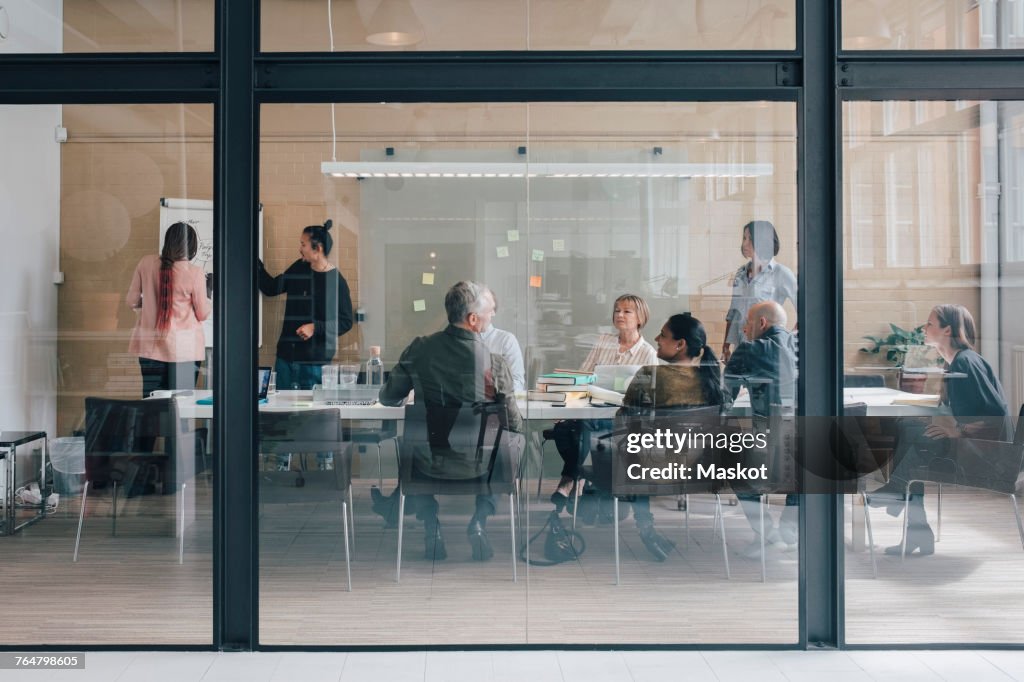 Multi-ethnic business team sitting in board room at office seen from glass