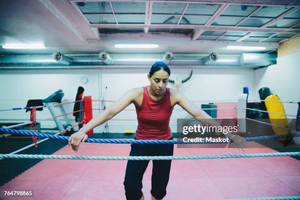 Mid adult female athlete leaning on boxing ring rope at health club