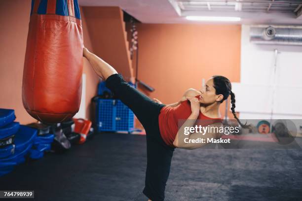 mid adult woman kicking punching bag at gym - kickboxing stock pictures, royalty-free photos & images