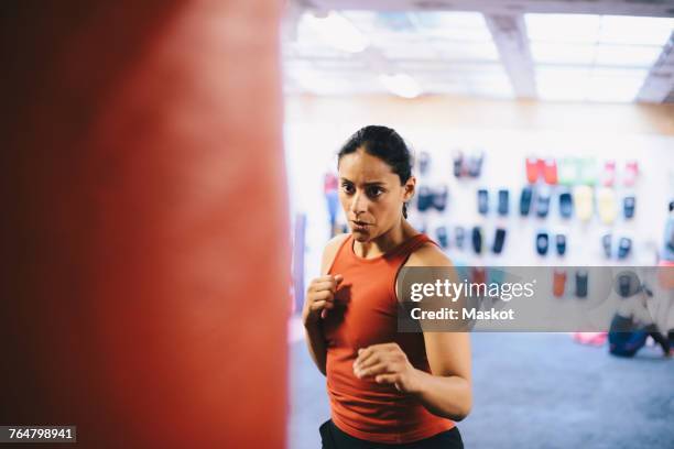 dedicated female athlete looking at punching bag in health club - fighting stance stock pictures, royalty-free photos & images