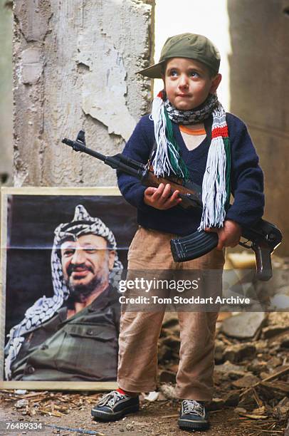 Palestinian boy poses with a rifle and a portrait of PLO chairman Yasser Arafat in the Bourj-el-Barajneh refugee camp, Beirut, 1989.