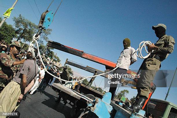 Iranian masked soldiers and government employees hold the rope while tightening the noose around the neck of a man sentenced to death among three...