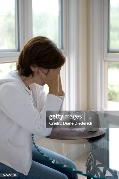 a woman, looking upset, sits at a kitchen table. - diane diederich stock-fotos und bilder