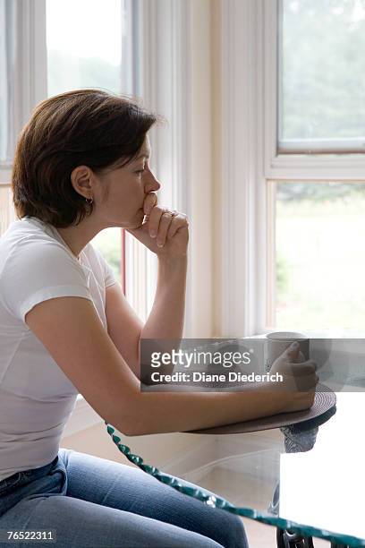 a woman, looking upset, sits at a kitchen table. - diane diederich stock-fotos und bilder