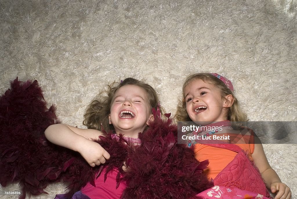 Two girls (2-4) dressed for a party, lying on rug.