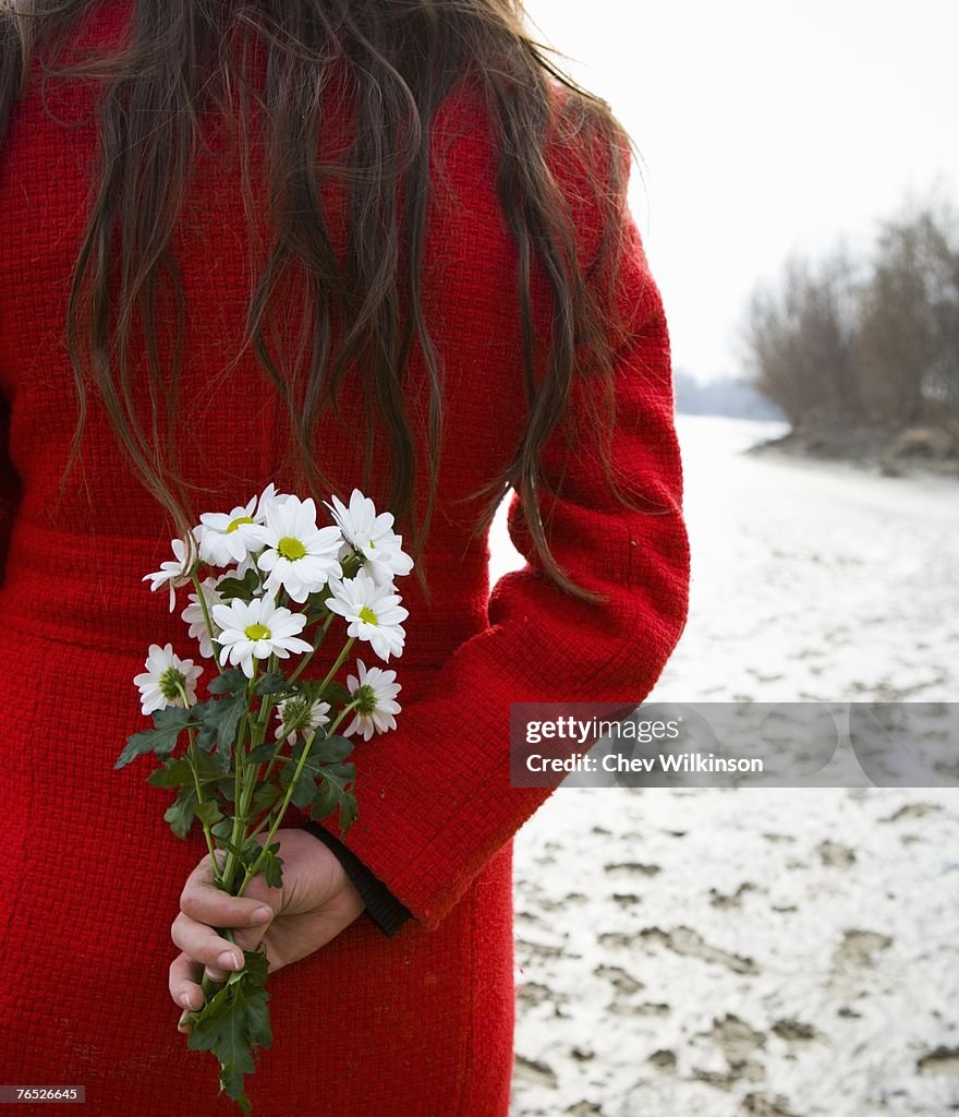 Young woman holding flowers behind back, rear, mid-section