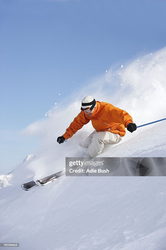 Man skiing down snow mountain slope sending up spray