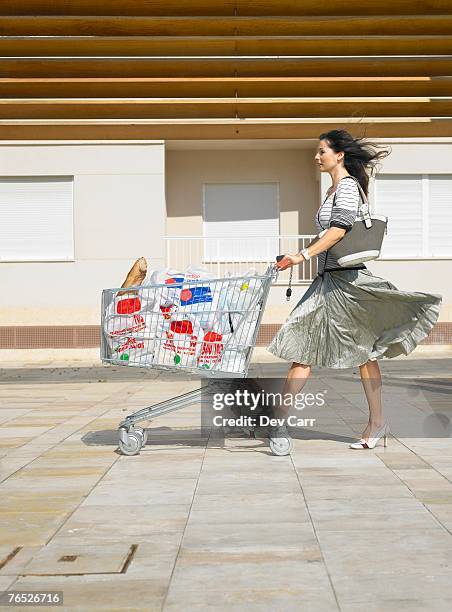 woman pushing supermarket trolley against wind, alicante, spain, - supermarket trolley female stock-fotos und bilder