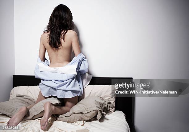 young woman on her knees in bed facing wall, wearing a mans shirt, rear view - surabaya stockfoto's en -beelden