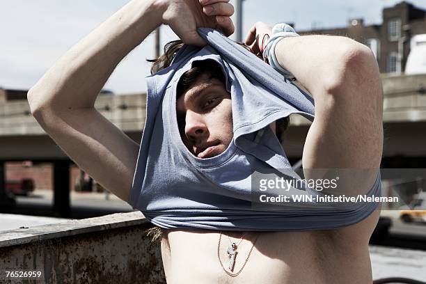 young man removing t-shirt, close-up, portrait - uitkleden stockfoto's en -beelden