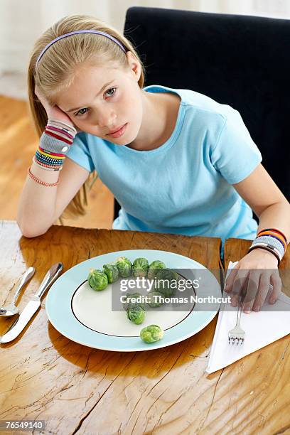 girl (9-11) sitting at plate of sprouts. portrait - ein mädchen allein stock-fotos und bilder