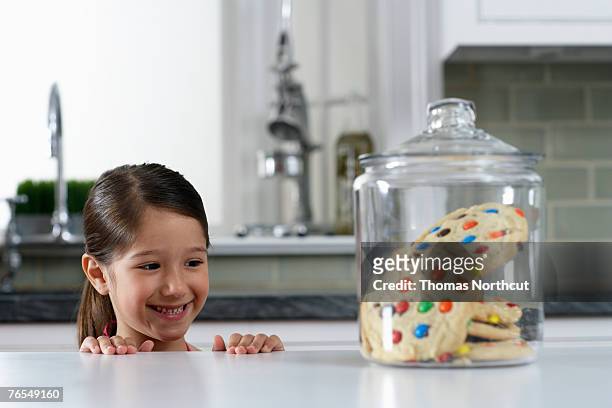 girl (4-6) looking at cookie jar on kitchen counter - child cookie jar stockfoto's en -beelden