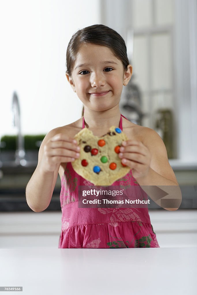 Girl (4-6) eating cookie, smiling, portrait