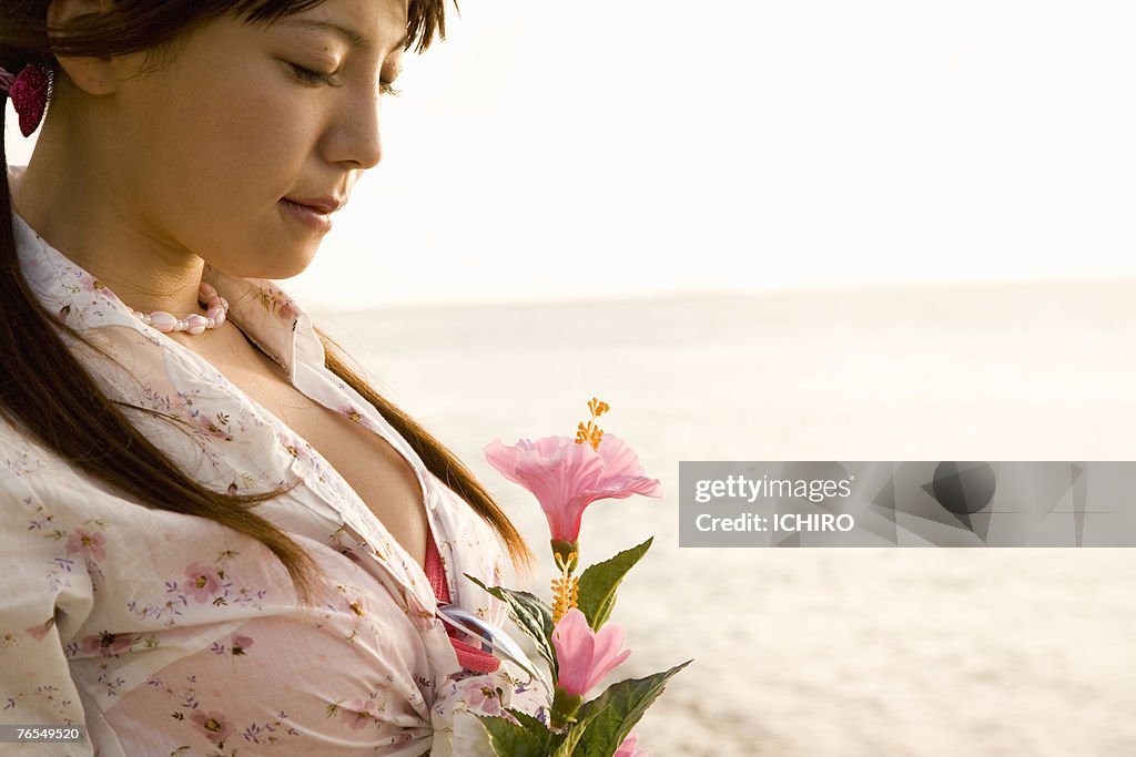 Young woman on beach, holding pink lily, close-up