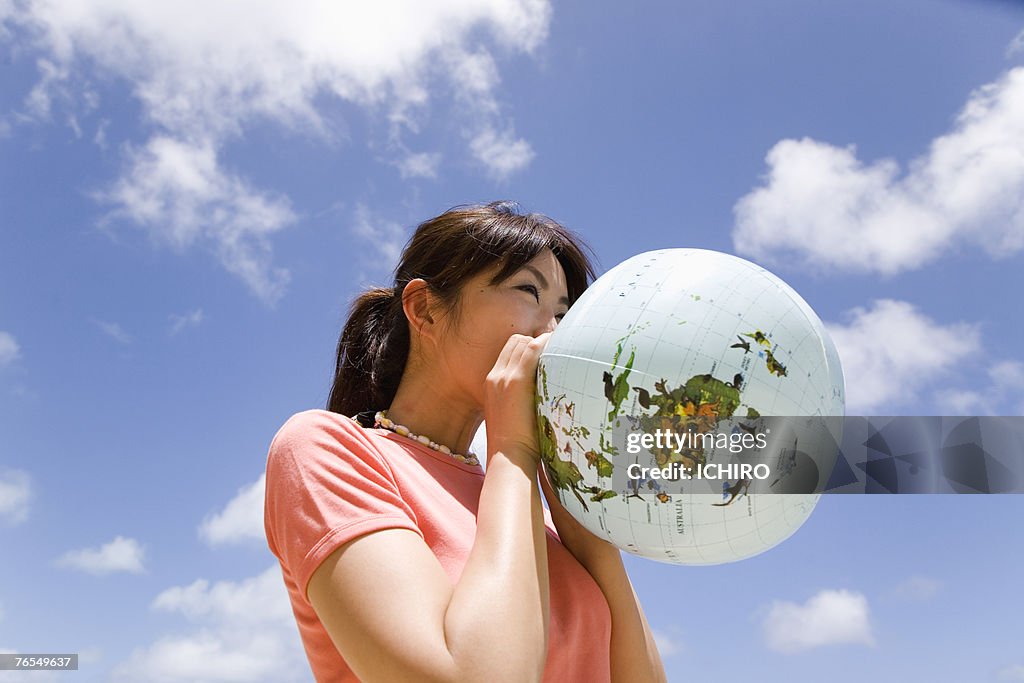 Young woman inflating balloon in form of Earth,outdoors,low angle view