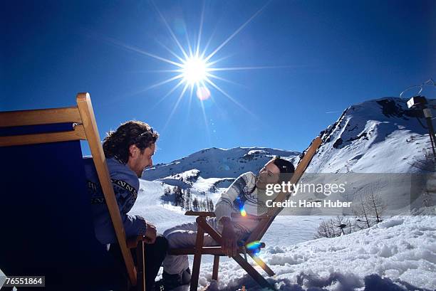 young couple sitting on deckchairs in alps, smiling - apres ski stock pictures, royalty-free photos & images