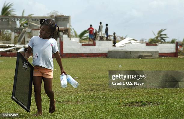 In this handout provided by the U.S. Navy, a young girl in an area affected by Hurricane Felix carries water bottles delivered by helicopters from...