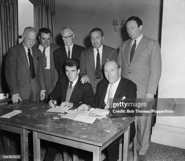 English footballer and former miner Bill Foulkes pictured seated on left with manager Matt Busby and other staff as he signs as a player for...