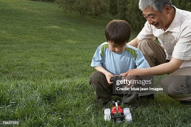an old man and a boy are playing with a remote control car. - remote control car games stockfoto's en -beelden